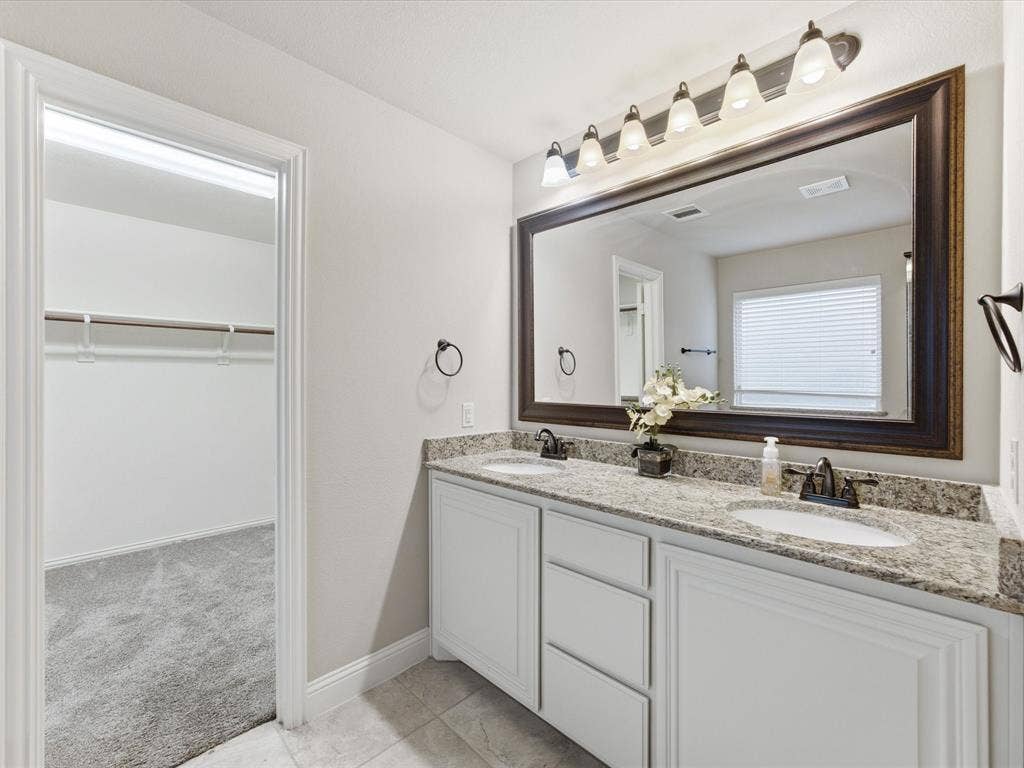 Double vanity featuring white cabinetry, stone-finish countertops, dual under-mount sinks, a large framed mirror, and five-bulb vanity lighting