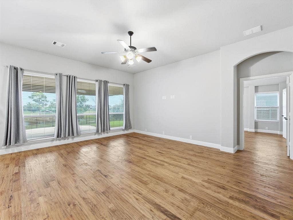 Spacious room featuring wood-finish flooring, a ceiling fan with integrated lighting, and multiple large windows