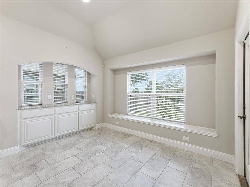 Vaulted ceiling featuring tile flooring, built-in cabinetry with stone-finish countertops, and an integrated window bench with a wide paneled window