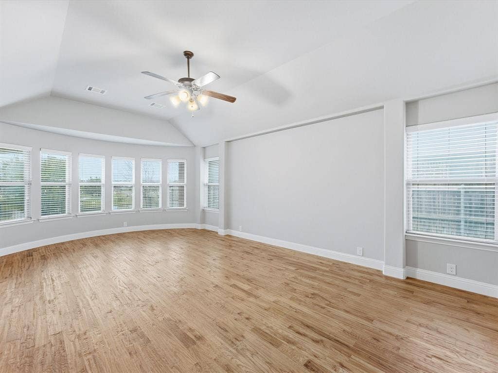 Vaulted ceilings, wood-finish flooring, numerous windows with integrated blinds, and a multi-blade ceiling fan with integrated lighting