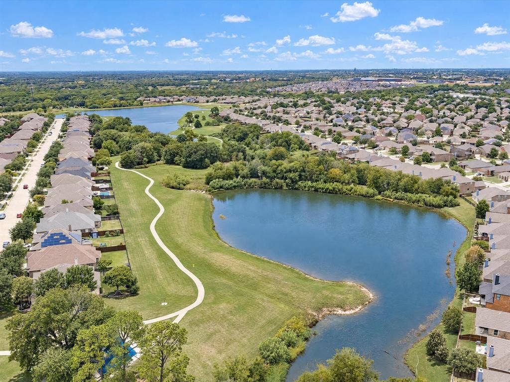Aerial perspective featuring a multi-acre pond, expansive green space, mature trees, and concrete walking paths
