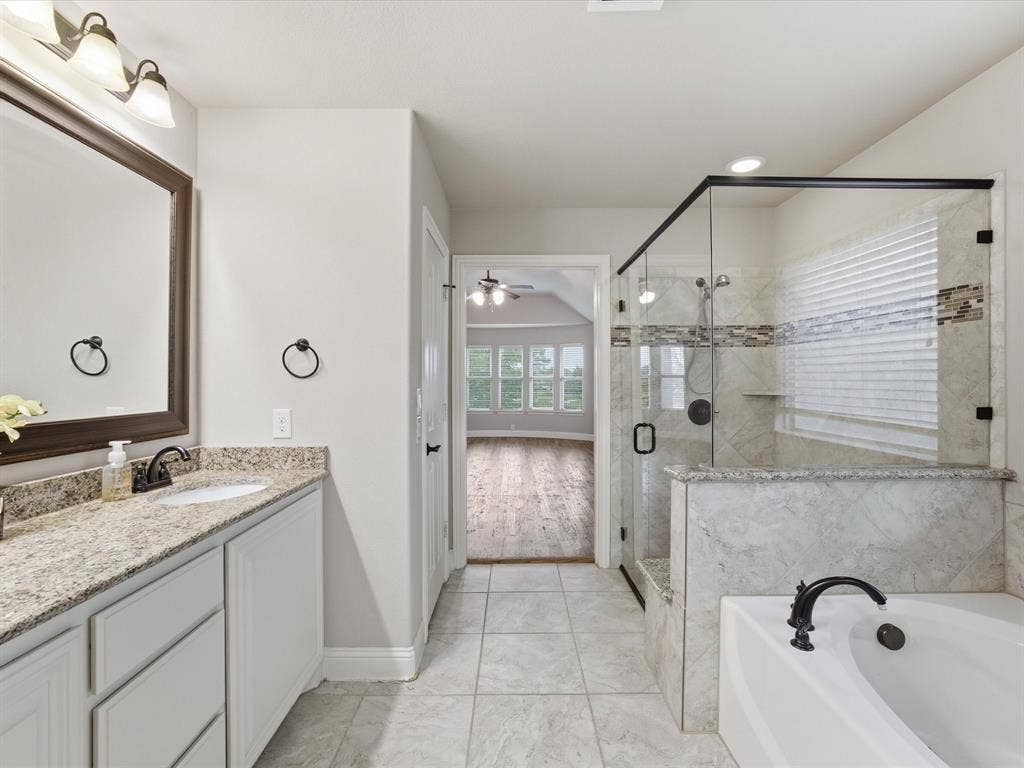 Bathroom featuring a stone-topped vanity, a glass-enclosed shower with decorative tile accents, and a deep soaking tub with matte black fixtures