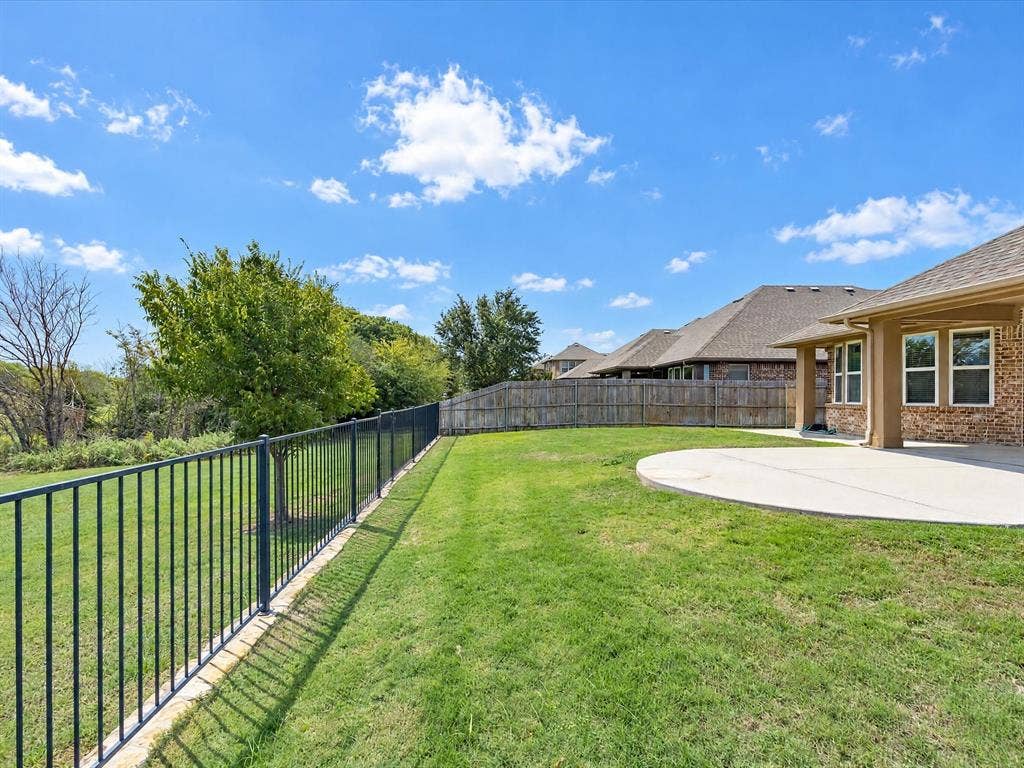 Expansive backyard featuring a concrete patio, perimeter metal fencing, and mature trees