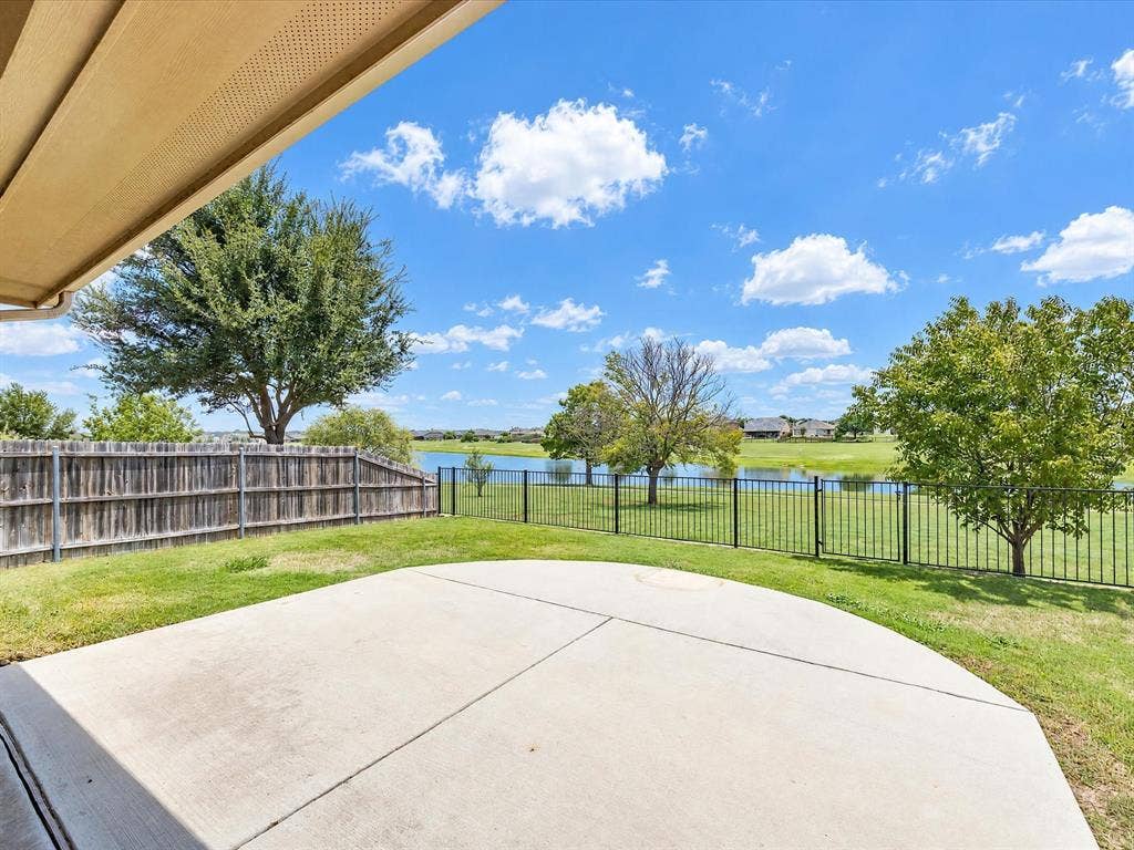Concrete patio overlooking a fenced backyard with water frontage and mature trees