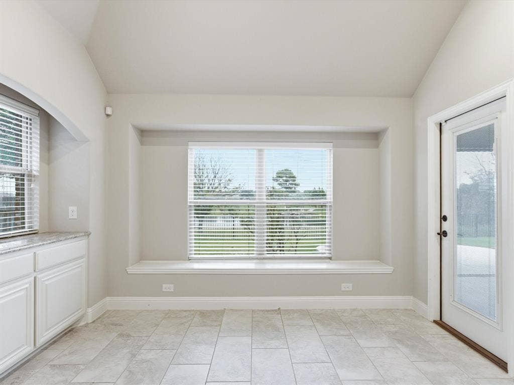 Vaulted ceilings featuring a window seat, light-toned stone flooring, built-in cabinetry with stone countertops, and a full-glass entry door