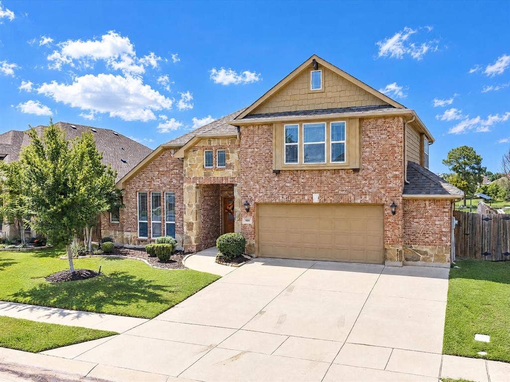 Two-story brick and stone veneer exterior featuring shake siding accents, a double-car garage, and a concrete driveway