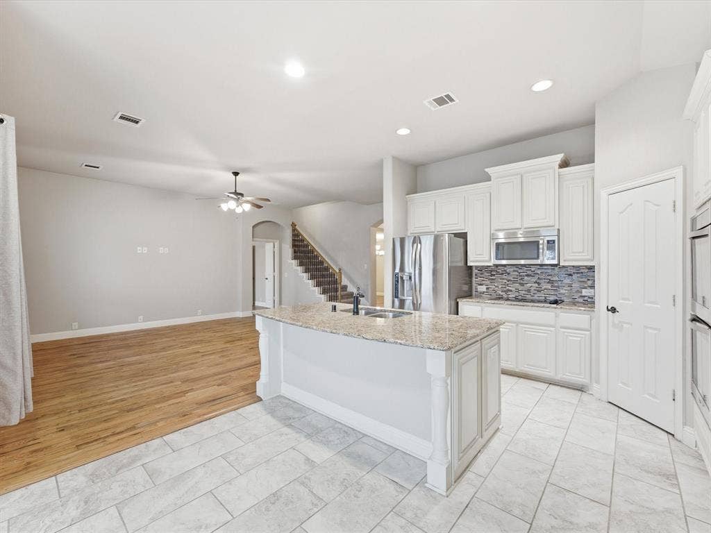 Kitchen featuring a central island with stone countertop, white cabinetry, tile backsplash, stainless steel appliances, and tile flooring
