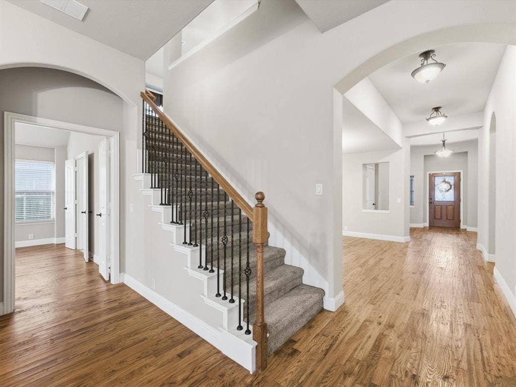 Foyer featuring wood-finish flooring, staircase with a wood handrail and iron balusters, arched architectural openings, and ceiling-mounted light fixtures