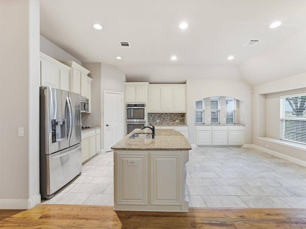 Kitchen featuring white cabinetry, stone-surface central island with undermount sink, stainless steel built-in double wall oven, patterned tile backsplash, and ceramic tile flooring