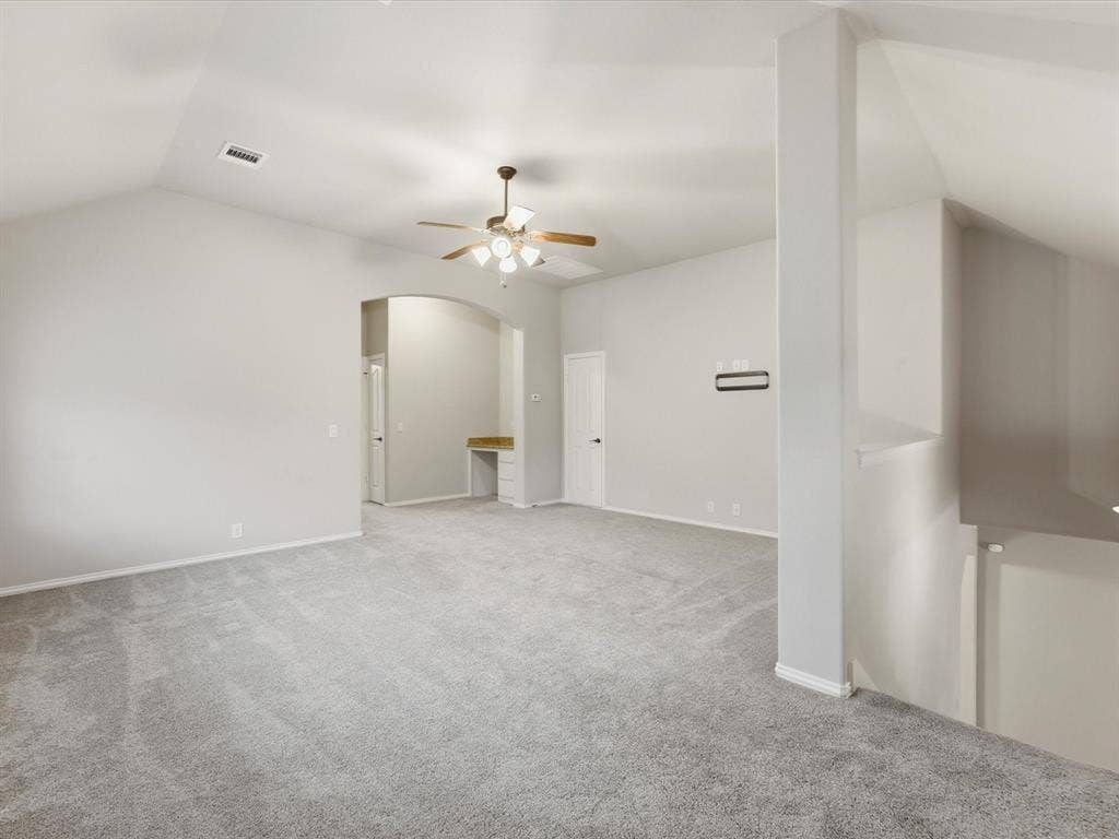 Vaulted ceilings featuring a central light-integrated ceiling fan, neutral wall-to-wall carpeting, and a recessed built-in desk with countertop