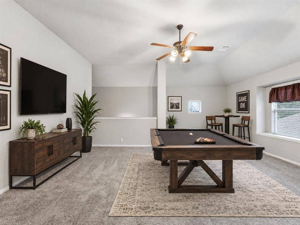 Vaulted ceilings, neutral carpeting, and a ceiling fan with integrated lighting