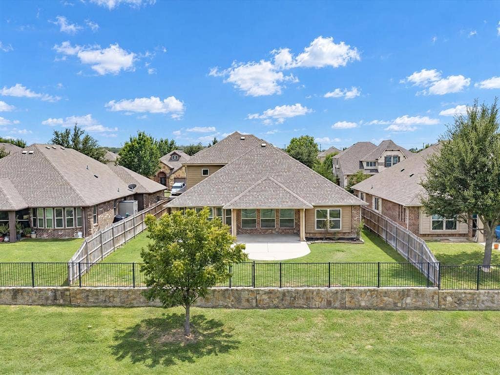 Exterior rear elevation featuring a multi-gable roofline, a covered concrete patio, a perimeter fence with metal railing, and a masonry retaining wall