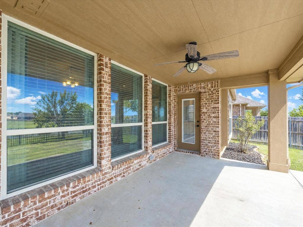 Covered patio featuring brick exterior walls, concrete flooring, a ceiling fan with integrated light fixture, and multiple large windows