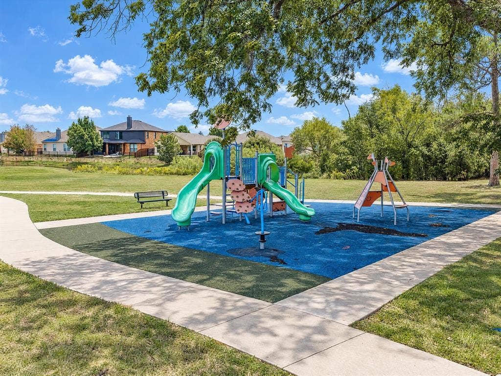 Outdoor recreation area featuring a multi-component play structure, poured-in-place rubber safety surfacing, concrete pedestrian pathways, and mature tree canopy