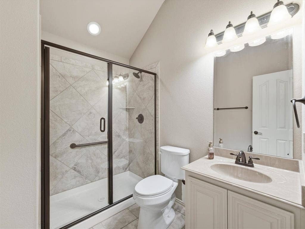 Bathroom featuring a glass-enclosed shower with tiled walls, vanity with an integrated sink, vaulted ceiling, and multi-bulb vanity lighting