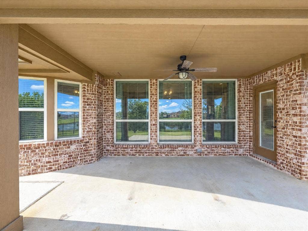Covered patio with a concrete floor, red brick exterior walls, multi-pane windows, and a ceiling-mounted fan with integrated light fixture