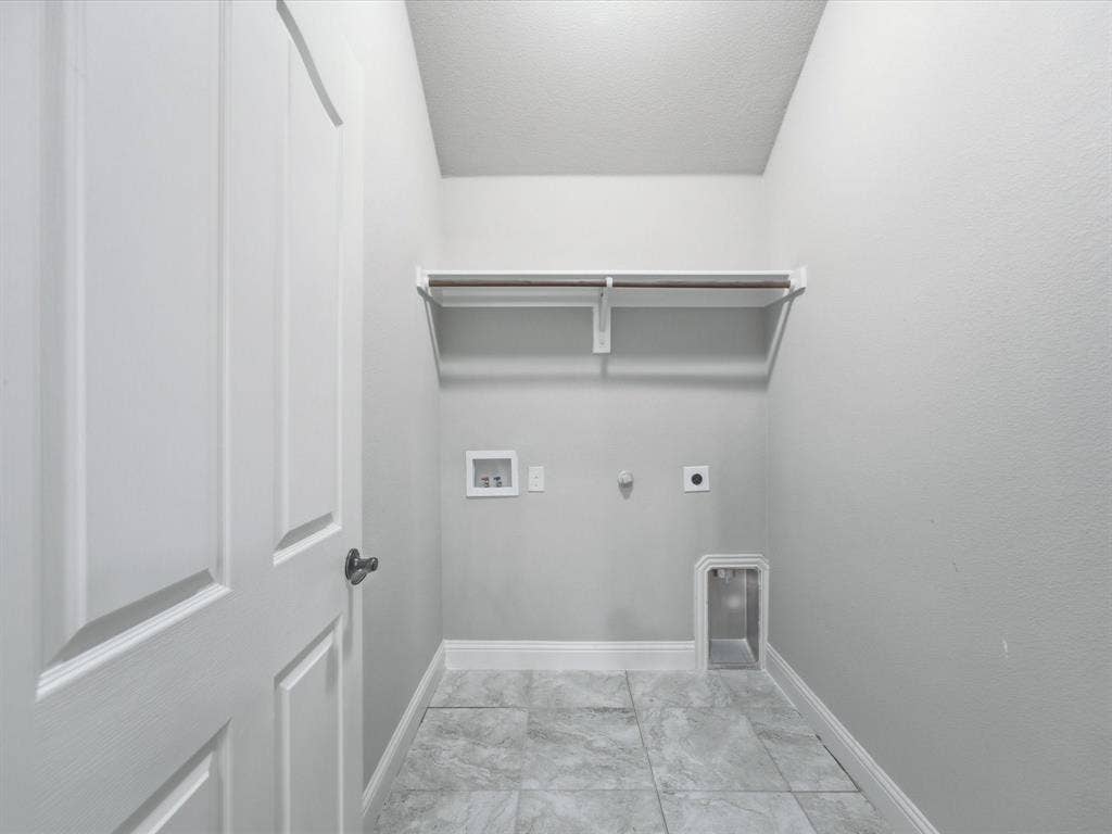 Utility area featuring large-format tile flooring, built-in shelving with integrated hanging rod, and dedicated hookups for laundry appliances