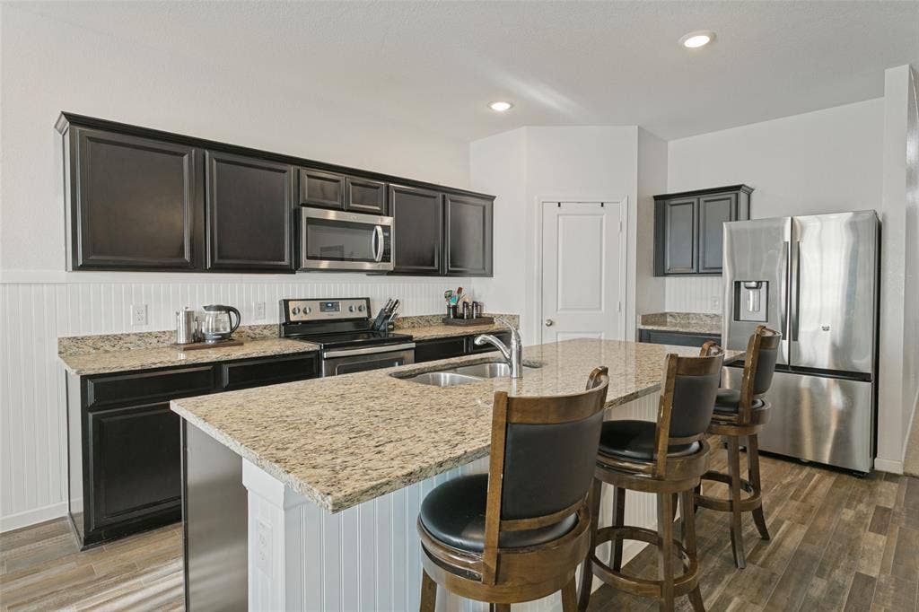 540 S Heights Drive, Crowley, TX 76036 Kitchen featuring dark cabinetry, stone-surface countertops, central island with stainless steel sink, beadboard backsplash, and wood-finish flooring