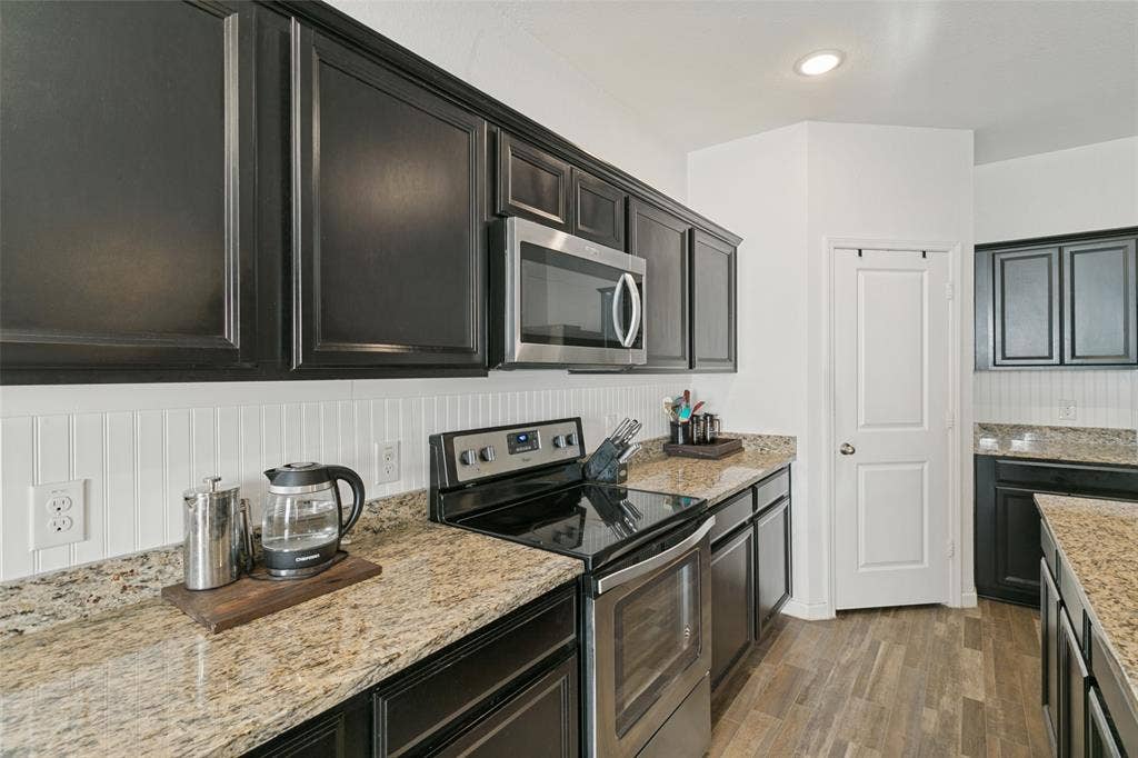 540 S Heights Drive, Crowley, TX 76036 Kitchen featuring black cabinetry, stone-finish countertops, beadboard backsplash, stainless steel appliances, and wood-finish flooring