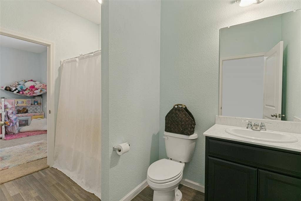 540 S Heights Drive, Crowley, TX 76036 Bathroom featuring a vanity with a white countertop and oval sink, a wall-mounted mirror, and wood-finish flooring