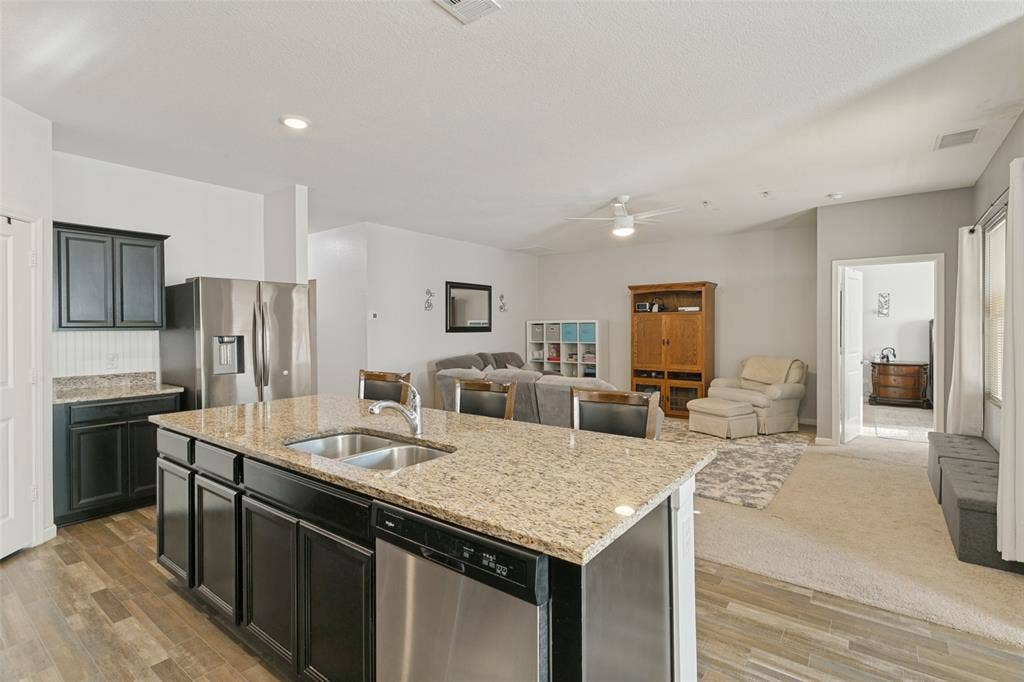 540 S Heights Drive, Crowley, TX 76036 Kitchen featuring a center island with a dual-basin stainless steel sink, granite countertops, dark-finish cabinetry, stainless steel appliances, and wood-finish flooring