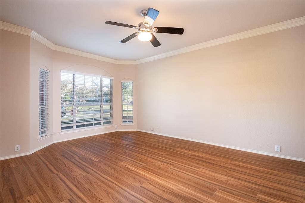 Expansive room featuring wood-finish flooring, a bay window with blinds, and ceiling fan
