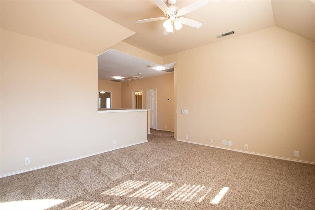 Vaulted ceiling with an integrated ceiling fan, neutral-toned carpet flooring, and a half-wall partition
