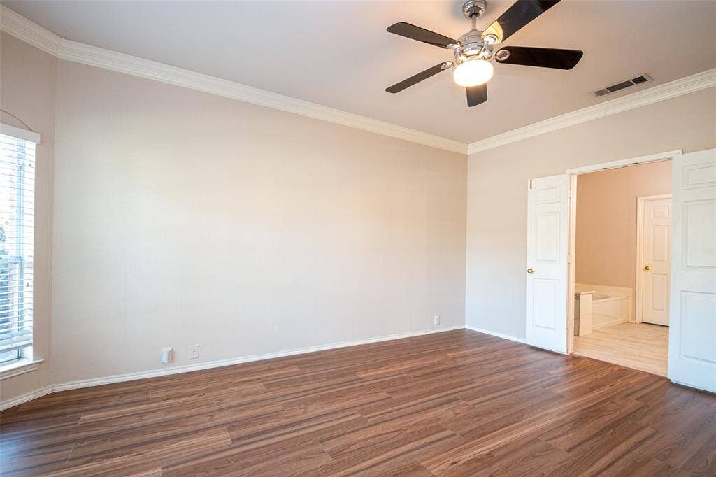 Spacious room with wood-finish flooring, crown molding, a ceiling fan, and double doors