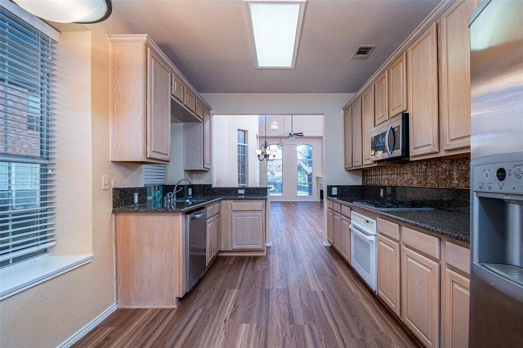 Galley-style kitchen featuring wood-finish flooring, wood cabinetry, dark countertops, and stainless steel appliances