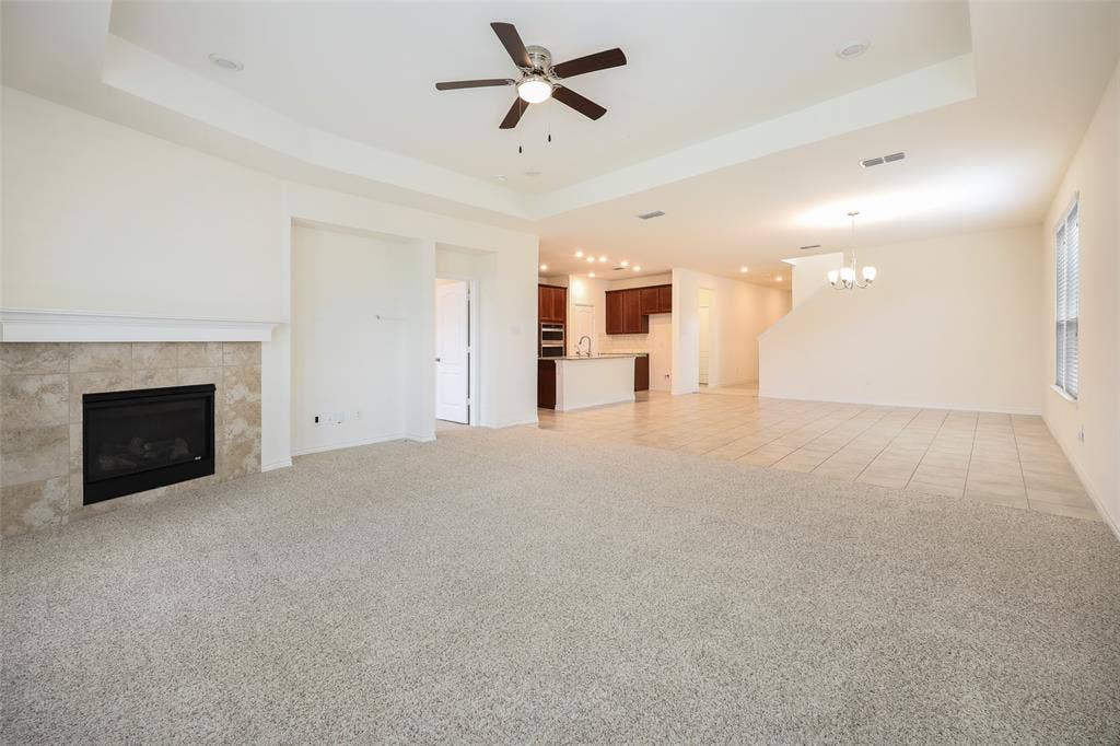 3681 Keechi Creek Drive, Celina, TX 75078 Tray ceiling featuring a central fan, tiled fireplace surround with a mantel, and neutral carpeting