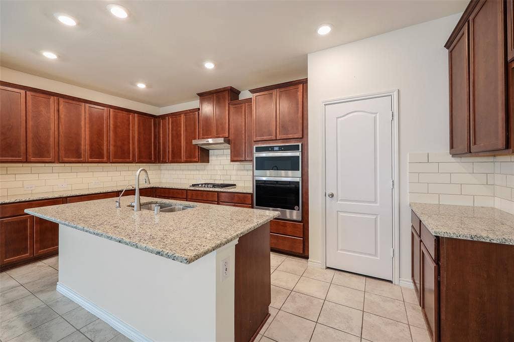 3681 Keechi Creek Drive, Celina, TX 75078 Kitchen featuring cherry-tone cabinetry, stone-surface countertops, subway tile backsplash, stainless steel built-in double wall ovens, and recessed lighting