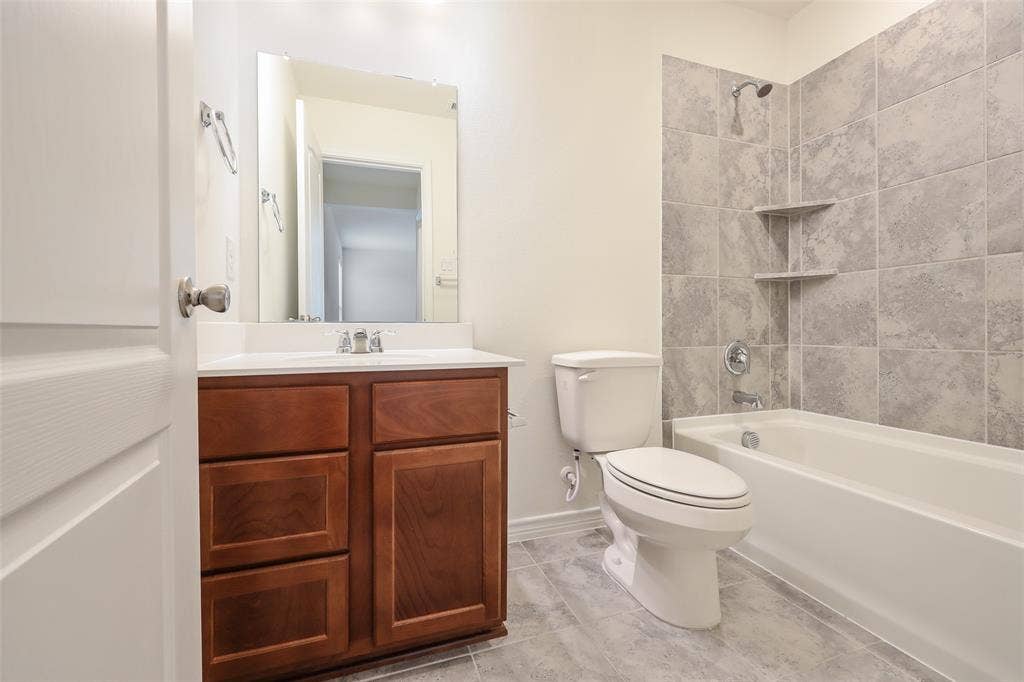 3681 Keechi Creek Drive, Celina, TX 75078 Bathroom featuring a wood-finish vanity with a white countertop, large wall-mounted mirror, tub-shower combination with gray tile surround, and built-in shelving
