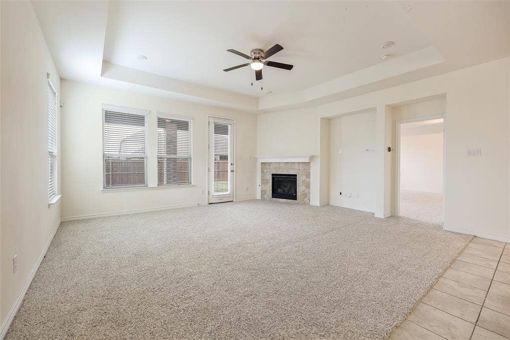 3681 Keechi Creek Drive, Celina, TX 75078 Living area featuring a tray ceiling, ceiling fan, carpeting, tiled fireplace surround, and access to exterior space