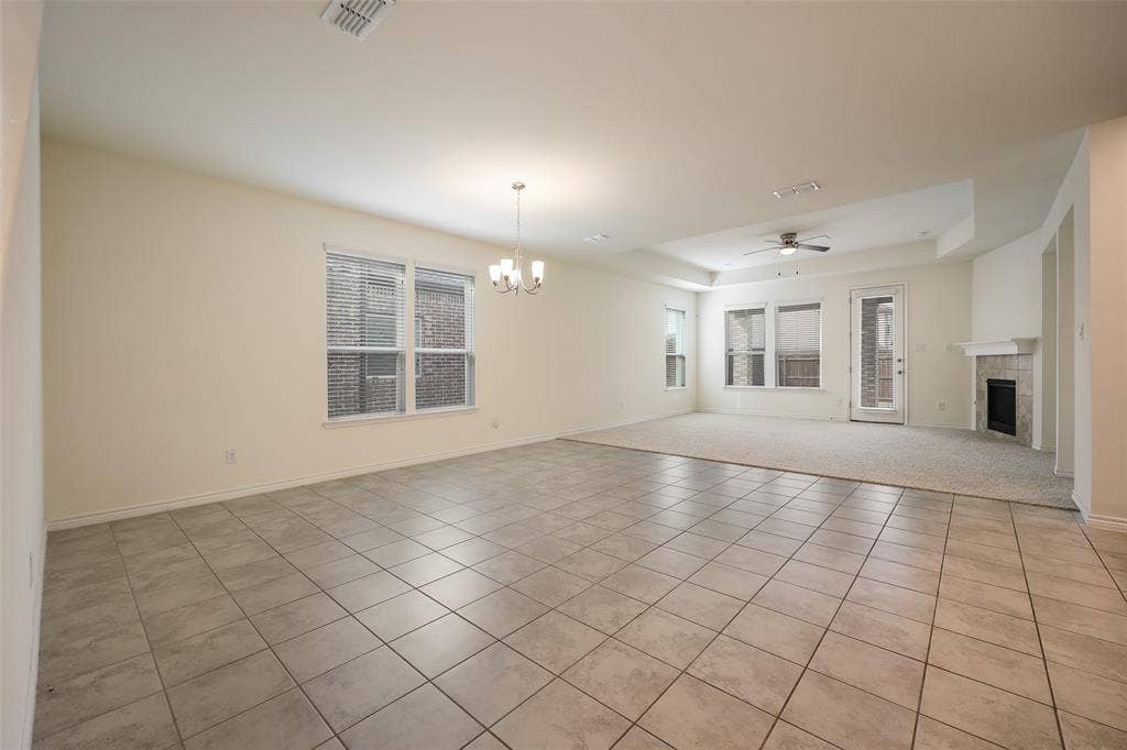3681 Keechi Creek Drive, Celina, TX 75078 Open-concept interior featuring large-format ceramic tile flooring, a multi-light chandelier, a recessed tray ceiling with a center fan, and a fireplace with a stone-surround mantel