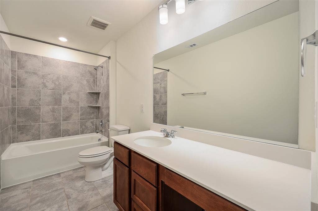 3681 Keechi Creek Drive, Celina, TX 75078 Bathroom featuring wood-finish cabinetry, a solid-surface vanity countertop, a large wall-mounted mirror, and tile-surround bathtub