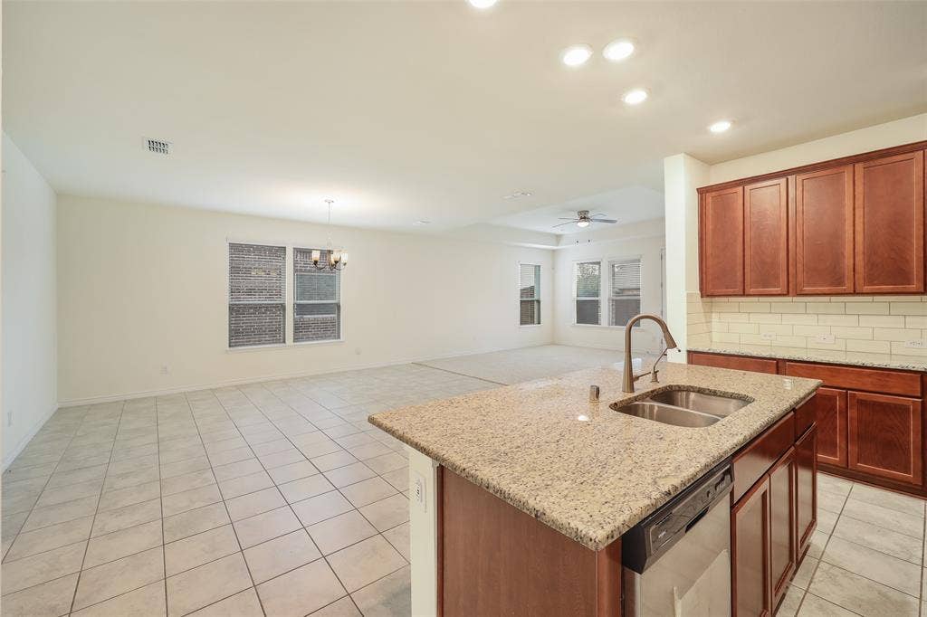 3681 Keechi Creek Drive, Celina, TX 75078 Kitchen featuring a center island, stone-finish countertops, stainless steel dual-basin sink, tile backsplash, and wood cabinetry