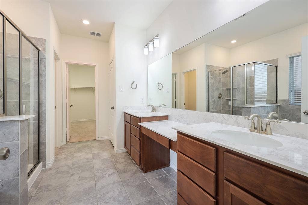 3681 Keechi Creek Drive, Celina, TX 75078 Dual-sink vanity with stone-finish countertops, wood cabinetry, glass-enclosed shower with tile surround, and full-width vanity mirror