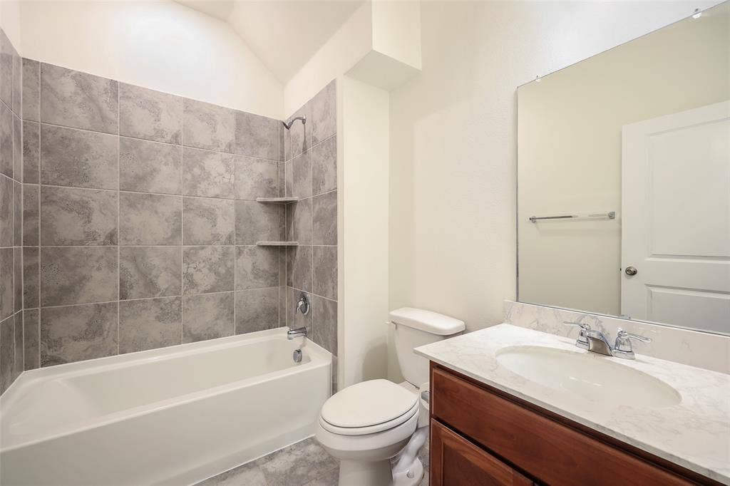 3681 Keechi Creek Drive, Celina, TX 75078 Full bathroom featuring a tub-shower combination with floor-to-ceiling tile surround, built-in shelving, wood-finish vanity with a stone-top integrated sink, and an expansive wall-mounted mirror