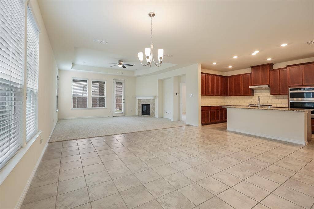 3681 Keechi Creek Drive, Celina, TX 75078 Open-concept area featuring ceramic tile flooring, built-in fireplace, tray ceiling, kitchen with dark wood cabinetry, and recessed lighting