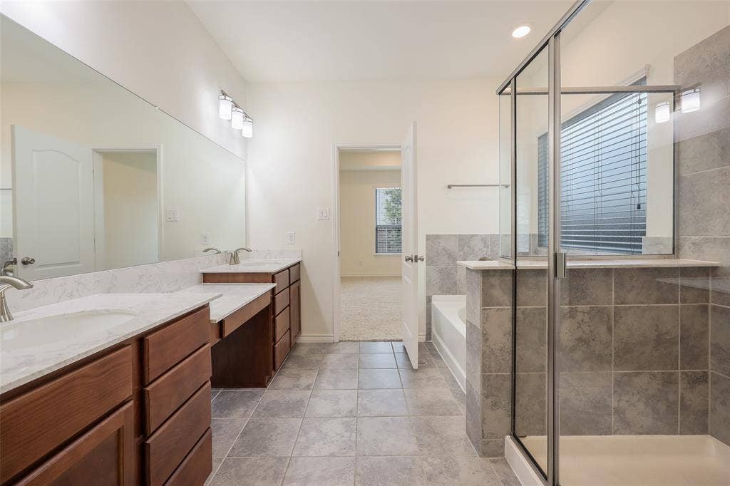 3681 Keechi Creek Drive, Celina, TX 75078 Dual vanity with solid-surface countertops, wood-finish cabinetry, tile flooring, and a glass-enclosed shower with tile surround