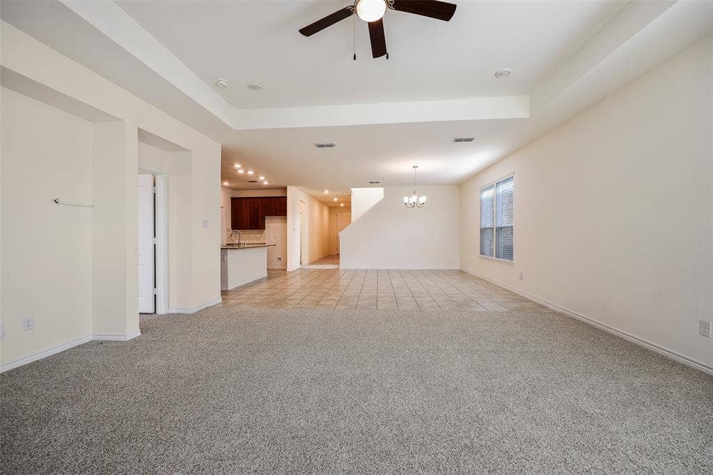 3681 Keechi Creek Drive, Celina, TX 75078 Tray ceiling featuring a central lighted ceiling fan, neutral wall-to-wall carpeting, large format tile flooring, recessed lighting, and kitchen cabinetry with a peninsula