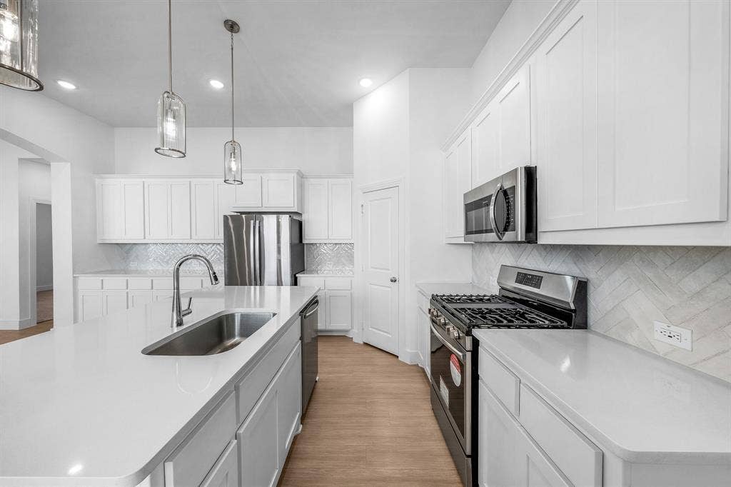 3800 Talisker Boulevard, Sherman, TX 75090 Kitchen featuring a large island with an undermount sink, white shaker cabinetry, stainless steel appliances, and wood-finish flooring