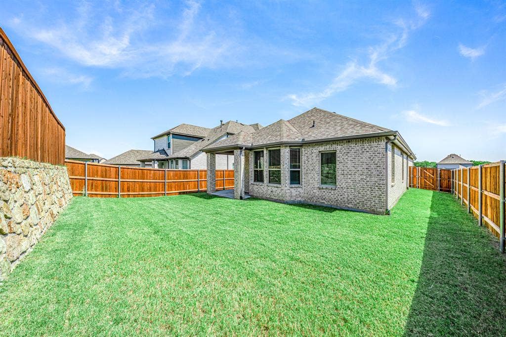 3800 Talisker Boulevard, Sherman, TX 75090 Expansive fenced backyard with a stone retaining wall, covered patio, and brick exterior