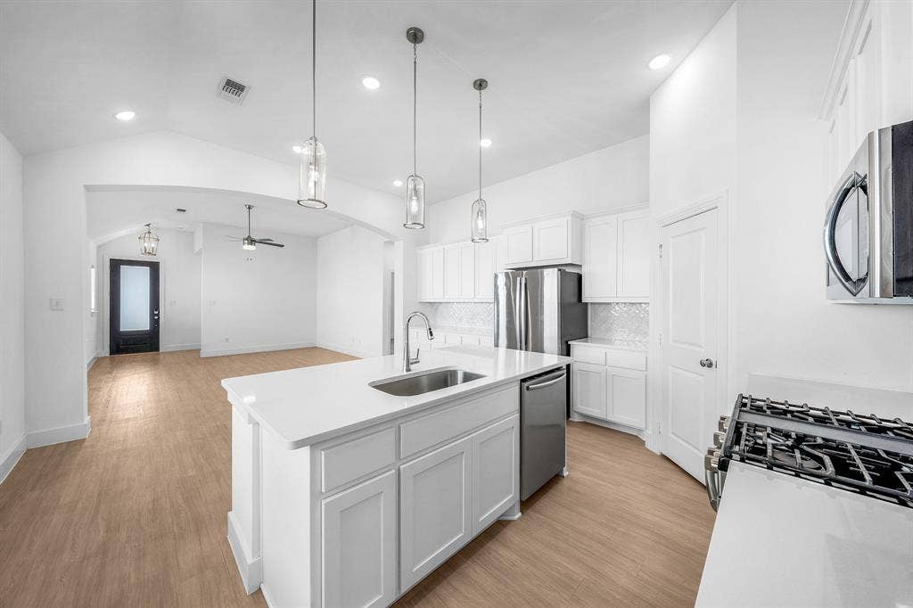 3800 Talisker Boulevard, Sherman, TX 75090 Open-concept kitchen featuring an island with an integrated sink, white cabinetry, stainless steel appliances, and wood-finish flooring