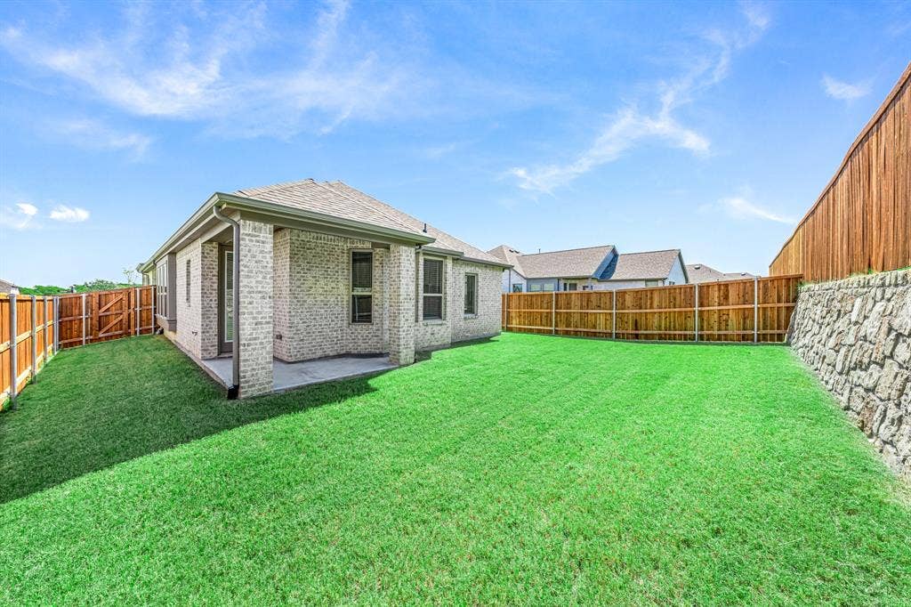 3800 Talisker Boulevard, Sherman, TX 75090 Expansive backyard featuring a lush lawn, privacy fencing, a stone retaining wall, and a covered patio with a brick exterior