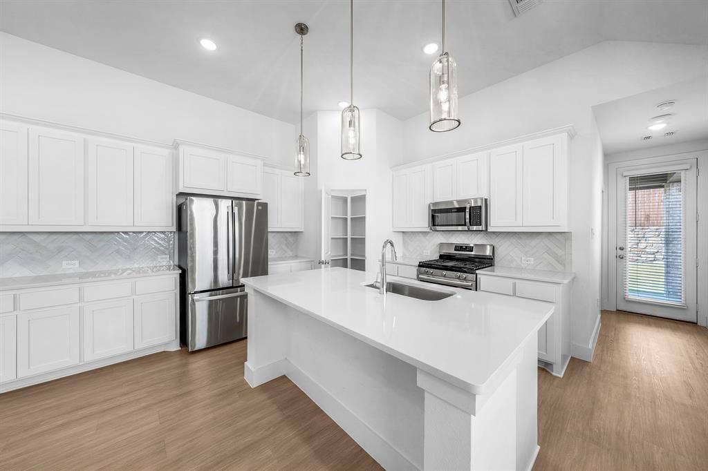 3800 Talisker Boulevard, Sherman, TX 75090 White cabinetry with brushed nickel hardware, stainless steel appliances, herringbone tile backsplash, and wood-finish flooring
