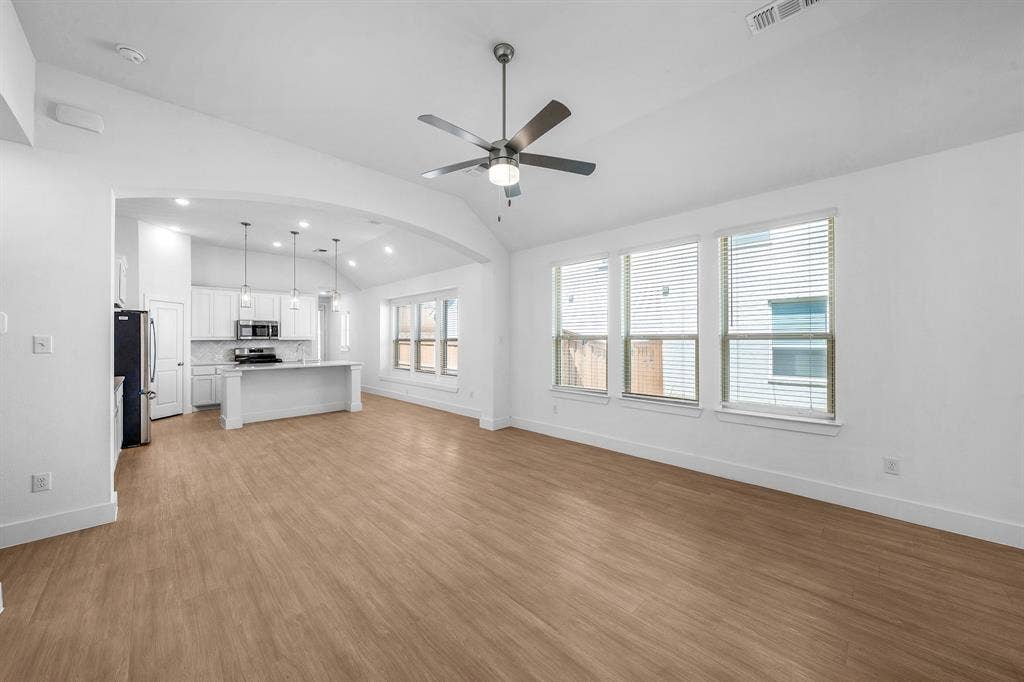3800 Talisker Boulevard, Sherman, TX 75090 Vaulted ceiling with a ceiling fan, wood-finish flooring, multiple windows, and an arched entryway to the kitchen