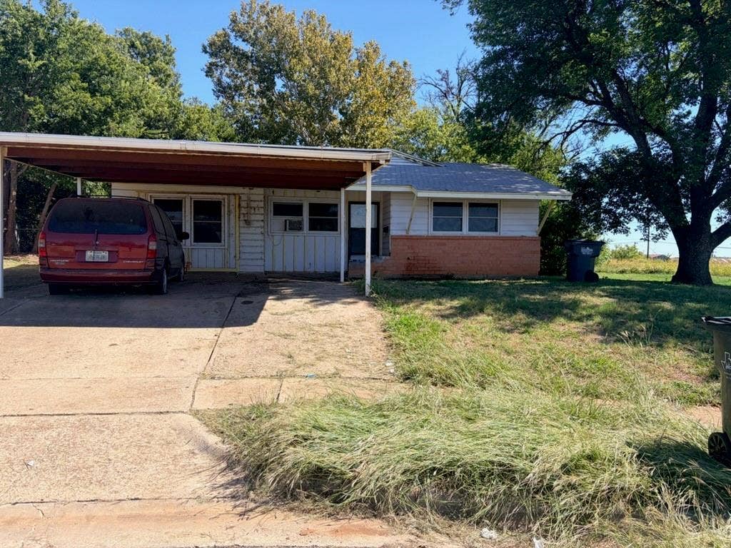 Carport with concrete driveway, mature trees, and brick detailing on the facade