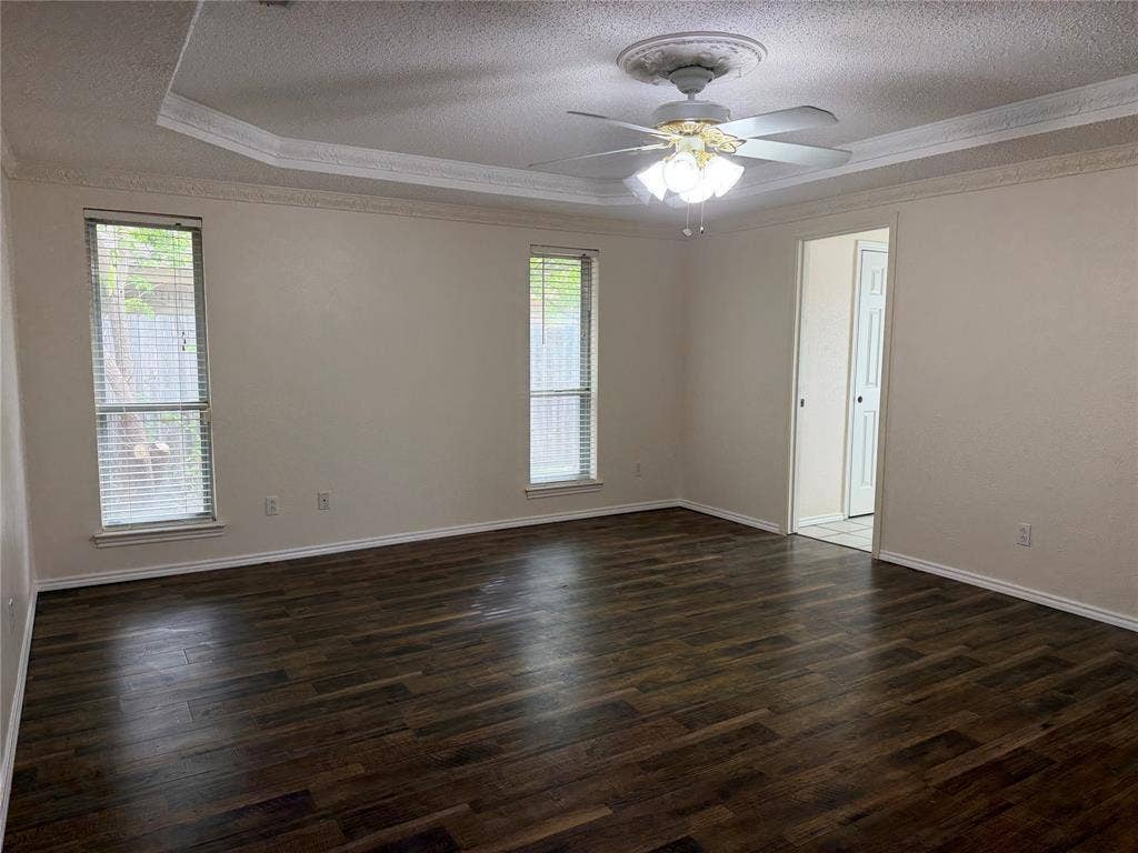 2408 Skiles Drive, Plano, TX 75075 Tray ceiling with crown molding, ceiling fan with light fixture, wood-finish flooring, and two windows with blinds
