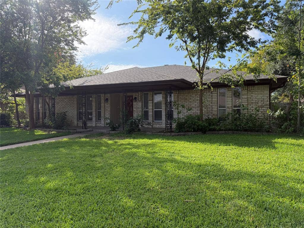 2408 Skiles Drive, Plano, TX 75075 Brick exterior with a covered front porch featuring decorative ironwork, a pitched shingle roof, and a mature tree canopy